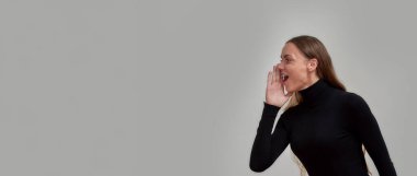 Siyah giyinmiş neşeli beyaz kadın gülümseyip çığlık atıyor, satış bilgilerini anlatıyor, gri arka planda izole bir şekilde poz veriyor.