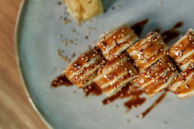 Geleneksel taze suşi rulosunu unagi ve susamlı bir tabakta servis et.