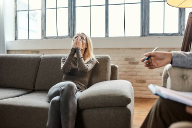Psikoterapistin yanındaki kanepede depresyonda olan beyaz bir kadın.
