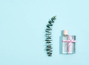 8 Mart için mükemmel bir hediye. Mavi arka planda yay ve yeşil yaprak dallı parfüm şişesi