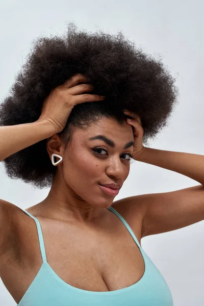 Portrait of young mixed race female model with afro hair looking at camera while posing isolated over light background