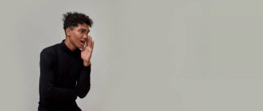 Siyahlar içinde piercing takmış genç adam gizli satış bilgilerini anlatırken yan tarafa bakıyor. Gri arka planda yalnız poz veriyor.