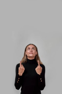 Siyah giyinmiş güzel beyaz bir kadın. Bir şey gösteriyor. Gri arka planda tek başına duruyor.