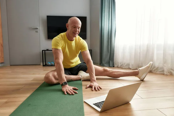 Yetişkin fitness, dizüstü bilgisayarda sanal fitness dersi alıyor. Kameraya bakıyor ve yoga minderinde otururken insanlara egzersiz tekniklerini anlatıyor. — Stok fotoğraf