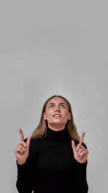 Siyah giyinmiş mutlu genç bayan, bir şey gösteriyor, gri arka planda tek başına duruyor.