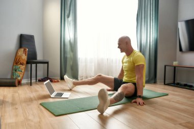 Çevrimiçi egzersiz. Oturma odasındaki yoga minderinde otururken online antrenman yapan olgun bir sporcu.