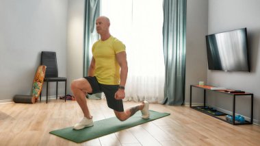 Gücümü arttırıyorum. Evde spor kıyafetleriyle egzersiz yapan olgun bir adam. Kafkas fitness eğitmeni, üniformalı antrenör oturma odasındaki yoga minderine çömelmiş.