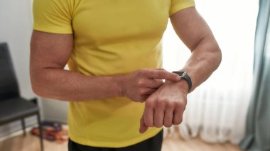 Bir sporcunun kırpılmış çekimi, spor saatini evde egzersiz yaparken ayarlayan fitness hocası.