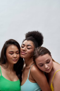 Renkli iç çamaşırlı üç kadının stüdyo portresi. Gözleri kapalı, açık arka planda poz veriyorlar.