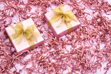 Karına, annene, kız kardeşine ya da kız arkadaşına hediyeler. İki küçük paketlenmiş hediye kutusunun üst görüntüsü. Pastel pembe arka planda altın yaylar ve dekoratif saman.