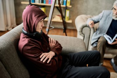 Elleri çapraz oturan rahatsız çocuk psikoterapistin yanında oturuyor.