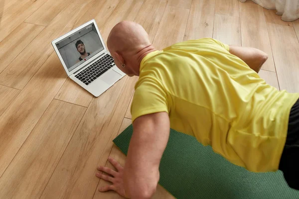 Залишайтеся придатними. Зрілий чоловік фітнес-інструктор в спортивному одязі робить поштовхи до йоги мат вдома, проводячи онлайн-тренінги, маючи віртуальний фітнес-клас — стокове фото