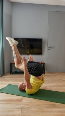 Güçlü ve odaklanmış erkek fitness koçu evde oturma odasında egzersiz yaparken bacağını kaldırıyor.