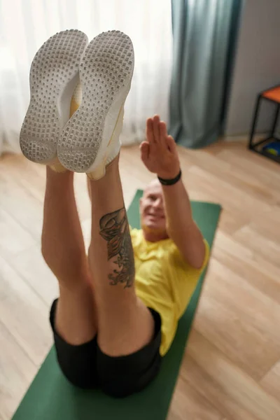 Fitness coach doing exercise on fitness mat, holding legs up while working out in living room at home. Focus on feet