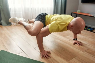Athletic strong man having training at home, standing on his arms and legs in the air. Hard yoga pose