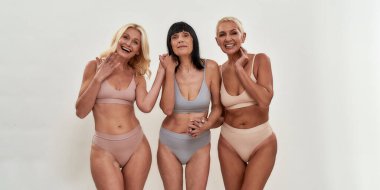 Feeling playful. Happy middle aged caucasian women in underwear holding hands together and smiling while standing on light background