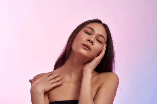 Looking and feeling gorgeous. Young sensual asian woman keeping eyes closed, touching her healthy soft face skin while standing against pink background — 스톡 사진