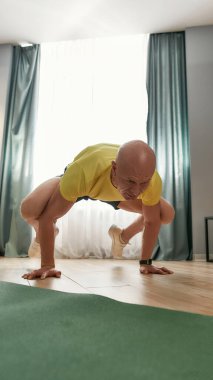 Güçlü fitness erkek antrenörü kolları ve bacakları havada, oturma odasında antrenman yaparken odaklanmış görünüyor.