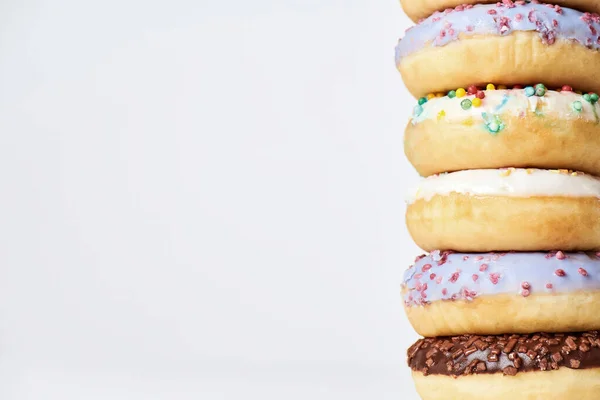 Desserts. Pile of different sweet colorful glazed donuts with colored sprinkles on light background