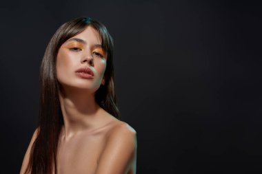 Renkli turuncu makyajlı, siyah arkaplanda izole bir şekilde poz veren sevimli esmer kadının güzel portresi.