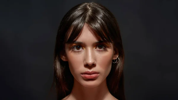 Beauty portrait of young brunette woman with brown eyes and colorful makeup looking at camera, posing isolated over black background