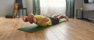 Evde yoga minderinde spor giyinen olgun bir adam, web afişi.