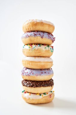 Sağlıksız tatlılar. Rengarenk donutlardan oluşan etkileyici bir kule serpiştirilmiş ve parlak arka planda izole edilmiş.