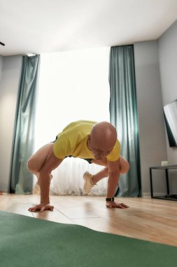 Spor salonu erkek koçu kolları ve bacakları havada dururken, evde egzersiz yaparken odaklanmış görünüyor.