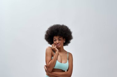 Afro saç stili, neşeli genç bir kadın mavi iç çamaşırı giyiyor, gülümsüyor, arka planda yalnız poz veriyor.