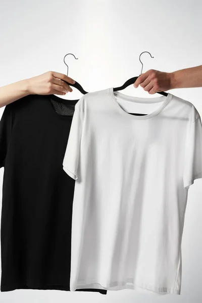 Black and white t-shirts on hangers against grey background