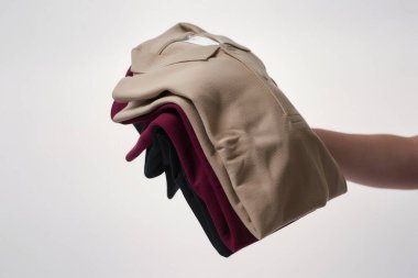 Erkek eli, gri arka planda çok renkli temel tişörtleri tutuyor.