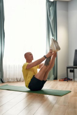 Aktif kel erkek fitness koçu, oturma odasında antrenman yaparken iki bacağını da havada tutuyor.