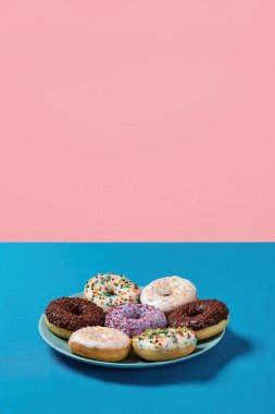 Abur cubur. Çeşitli renkli yuvarlak donutların yakın plan çekimleri. Üzerinde mavi arkaplan üzerine serpiştirilmiş şekerler var.