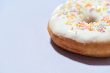 Şeker bağımlılığı. Yakın plan çekimde taze pişmiş lezzetli donut renkli serpiştirilmiş ve mor arka planda beyaz şeker jöleli.