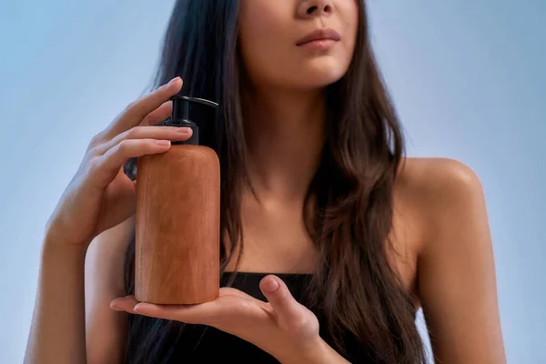 Pielęgnacja. Przycięte zdjęcie młodej azjatyckiej kobiety trzymającej produkt kosmetyczny na niebieskim tle — Zdjęcie stockowe