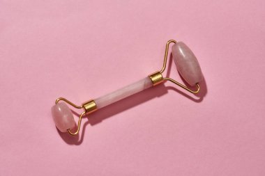 Gül kuvars yüz masajı aracının üst görüntüsü pembe arka planda izole edilmiş.