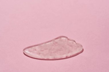 Gül kuvars yüz masajı yakın çekim Gua Sha kazıyıcı pembe arka planda izole