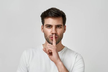 Ağzını kapatan tişörtlü genç sakallı adam.