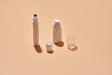 Beyaz plastik pompa şişesi ve göz silindirli cilt bakım ürünü için tüp bej arka planda yansıma ile izole