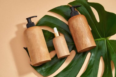 Çevre dostu, pompalı ahşap şişeler ve bej arka planda yeşil tropikal bitkilerin üzerine bırakılan damlalar.