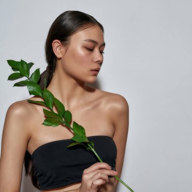 Elinde bitki tutan, siyah bluzlu, muhteşem, yarı çıplak Asyalı bir kızın portresi.