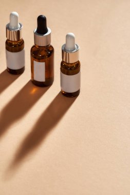 Bej arka planda izole edilmiş üç cam şişe kozmetik ürününün yakın çekimi.