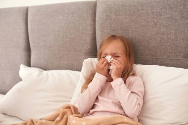 Genç bir kızın yatağın üstünde burnunu sildiği bir resim.