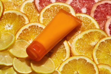Plastik turuncu tüp ile doğal C vitamini cilt bakımı ürününü kapatın. Taze sulu turuncu turunçgil dilimlerinin arka planında izole edilmiş.