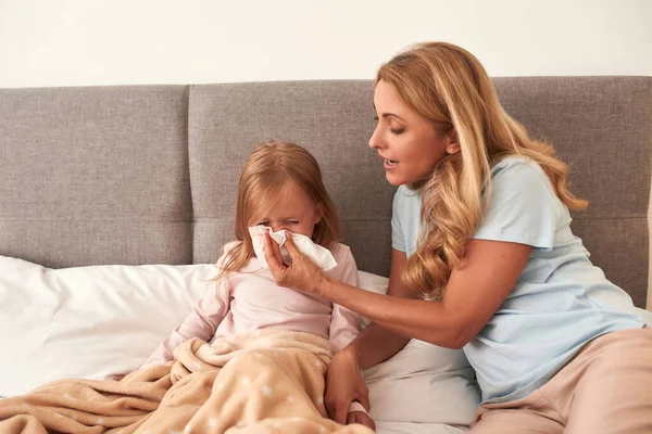 En bild på en mor som blåser sin barnnäsa och tar hand om henne. — Stockfoto