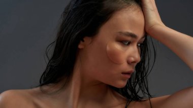 Kozmetik göz bantları ve ıslak saçlarıyla genç ve güzel bir Asyalı yarı çıplak kadın.