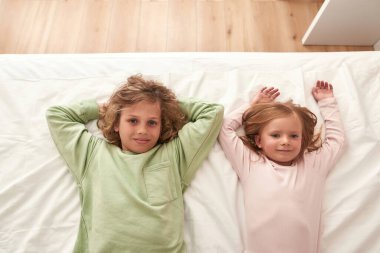 Erkek ve kız kardeş yatakta takılıyor, kameraya bakıyor.