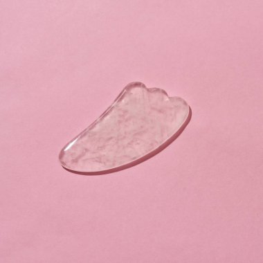 Gül kuvars yüz masajı yakın çekim Gua Sha kazıyıcı pembe arka planda izole