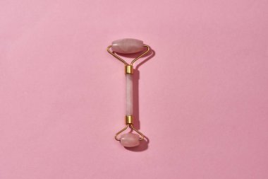 Gül kuvars yüz masajı aracının üst görüntüsü pembe arka planda izole edilmiş.