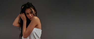 Genç ve güzel Asyalı yarı çıplak kadın kameraya bakıyor ve saçına banyo havlusuyla dokunuyor. 